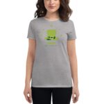A woman stands wearing a gray t-shirt featuring a green leprechaun hat design surrounded by small green clovers with the text CHEERS HAPPY ST PATRICKS DAY on it