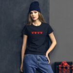 A young woman stands against a textured dark wall wearing a black shirt with the word LOVE in red hearts and a dark knit beanie while casually posing with one hand on her hip.