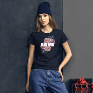 A young woman leans against a dark background wearing a black shirt with floral designs and the word LOVE while dressed in casual jeans and a blue beanie.