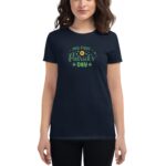 A woman is wearing a navy blue t-shirt featuring the text "my first St. Patrick's Day" in green with decorative elements  standing against a neutral background.