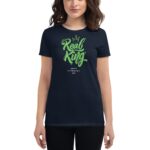 A woman stands wearing a dark t-shirt featuring bold green text that reads "Real King" with a crown graphic above and "Happy St. Patrick's Day" below in smaller print.