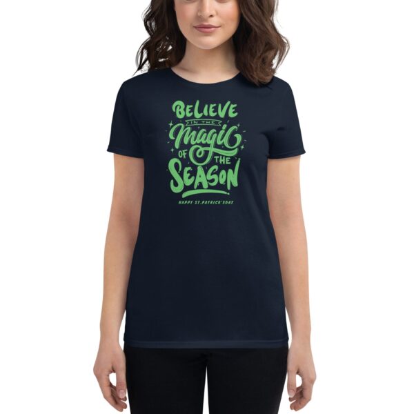 A woman is wearing a dark t-shirt featuring green text that reads Believe in the Magic of the Season Happy St. Patrick's Day creating a festive holiday-themed appearance.