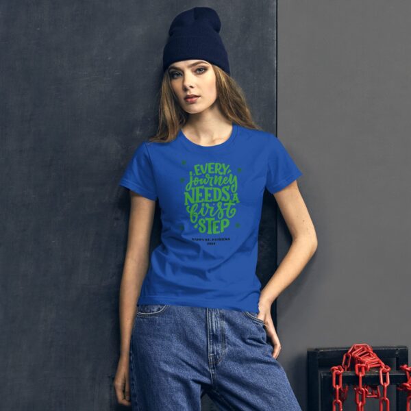 A person wears a blue shirt with green text that reads every journey needs a first step happy st patricks 2022 against a dark textured background with chains visible.