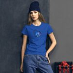 A young woman stands confidently wearing a blue t-shirt with a heart design featuring flowers. She has long hair and is wearing a black beanie in a modern  urban setting.