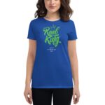 A woman wears a blue t-shirt with green text that reads "Real King" above "Happy St. Patrick's Day" showcasing festive attire in a casual setting.