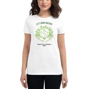 A woman is wearing a white t-shirt featuring a graphic of hands holding a globe surrounded by leaves with the text LET'S GROW TOGETHER HAPPY ST. PATRICKS 2024