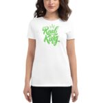 A woman stands wearing a white t-shirt with green stylized text saying "Real King" accompanied by a small crown graphic above the text  set against a plain background.