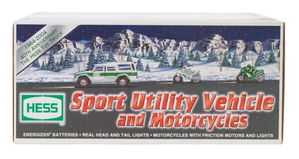 A toy sport utility vehicle and two motorcycles are displayed on a snowy landscape box art with evergreen trees and mountains in the background featuring the text HESS Sport Utility Vehicle and Motorcycles Energizer batteries real head and tail lights motorcycles with friction motors and lights 1964-2004 40th anniversary the Hess toy truck.