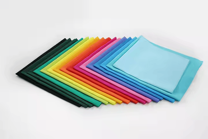 Solid color bandanas neatly stacked side by side, showcasing a range of vibrant hues in an organized, horizontal layout.