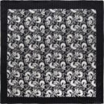 A patterned fabric displays an intricate design of alternating skulls and swirling elements in black and white  creating a striking visual effect against a black background.