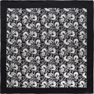 A patterned fabric displays an intricate design of alternating skulls and swirling elements in black and white  creating a striking visual effect against a black background.