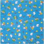A blue patterned fabric features colorful cartoon bunnies eggs and chicks scattered throughout the design creating a festive spring theme. The vibrant colors and playful motifs suggest a cheerful atmosphere.