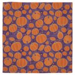 A vibrant purple fabric covered in a pattern of various orange pumpkins with some swirling vines and small circles creating a festive autumnal atmosphere.