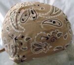 A beige bandana is displayed  featuring a paisley pattern in black and white. It is positioned on a mannequin head against a light background  highlighting its textile design and shaping.